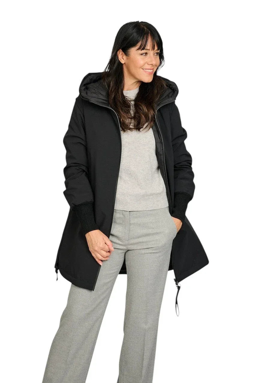 Vrouw in een zwarte jas met capuchon, grijze trui en een grijze pantalon.