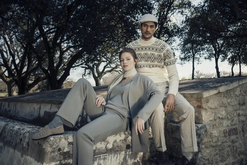 Man in beige gebreide trui en vrouw in grijs ensemble poseren buiten.