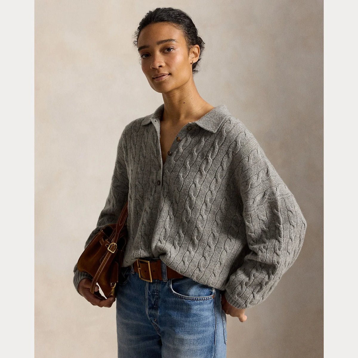 Vrouw in een grijze kabelgebreide cardigan met kraag en een blauwe spijkerbroek.